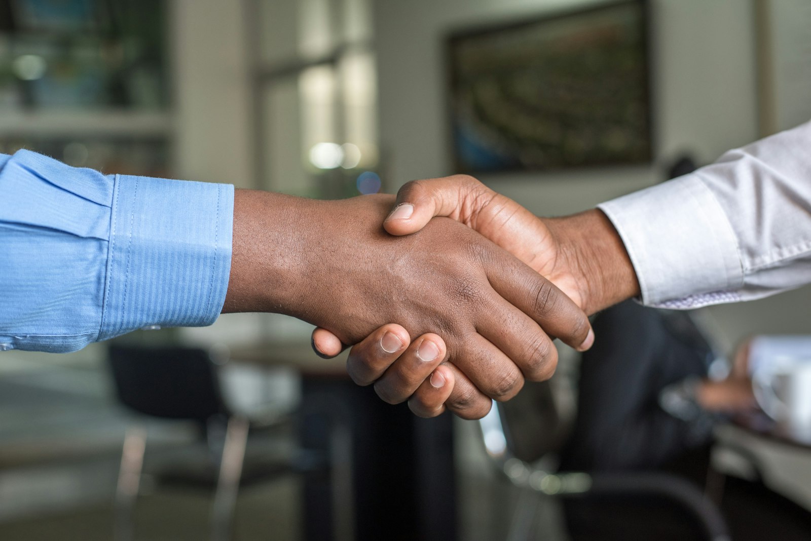 Two corporate executives shaking hands across a desk after agreeing the headline terms of a UK subsidiary divestment.